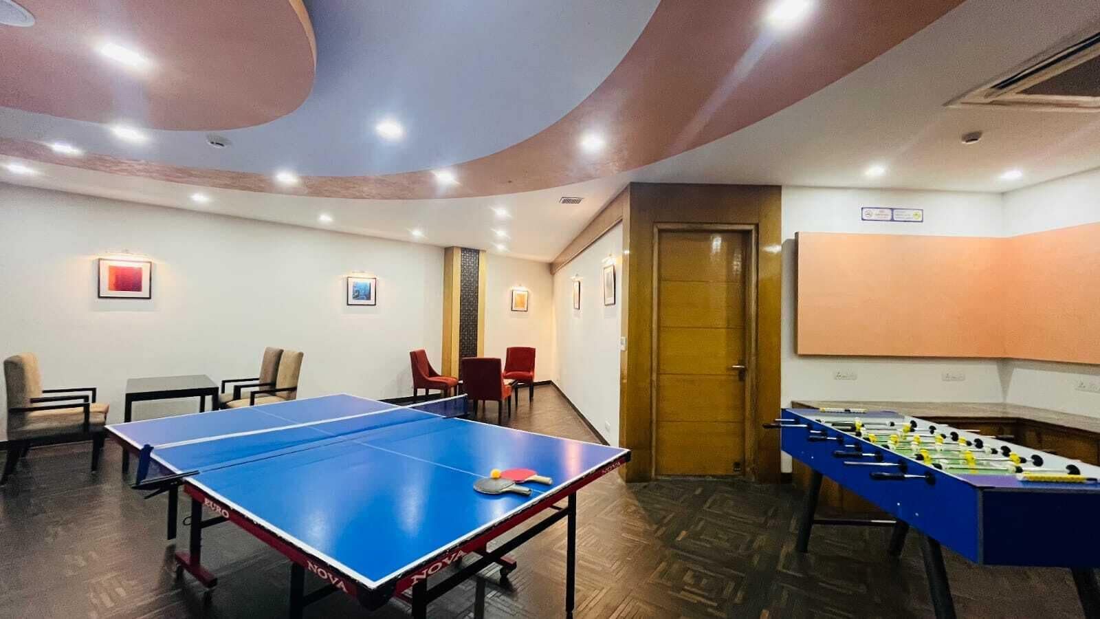 A room with a ping pong table, a foosball table, and several chairs.