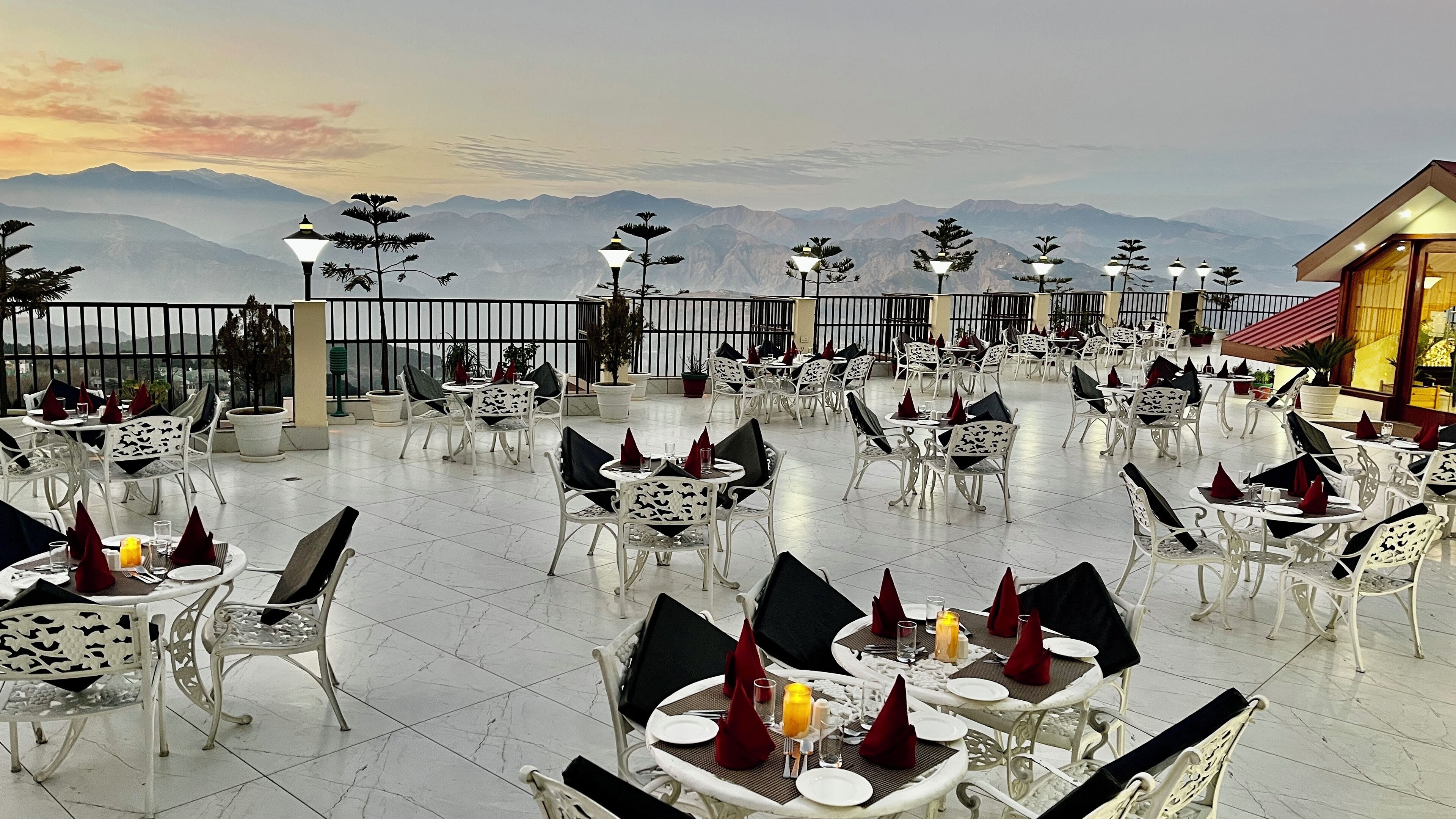Um restaurante no terraço com mesas e cadeiras dispostas para refeições, com vista para uma paisagem montanhosa.