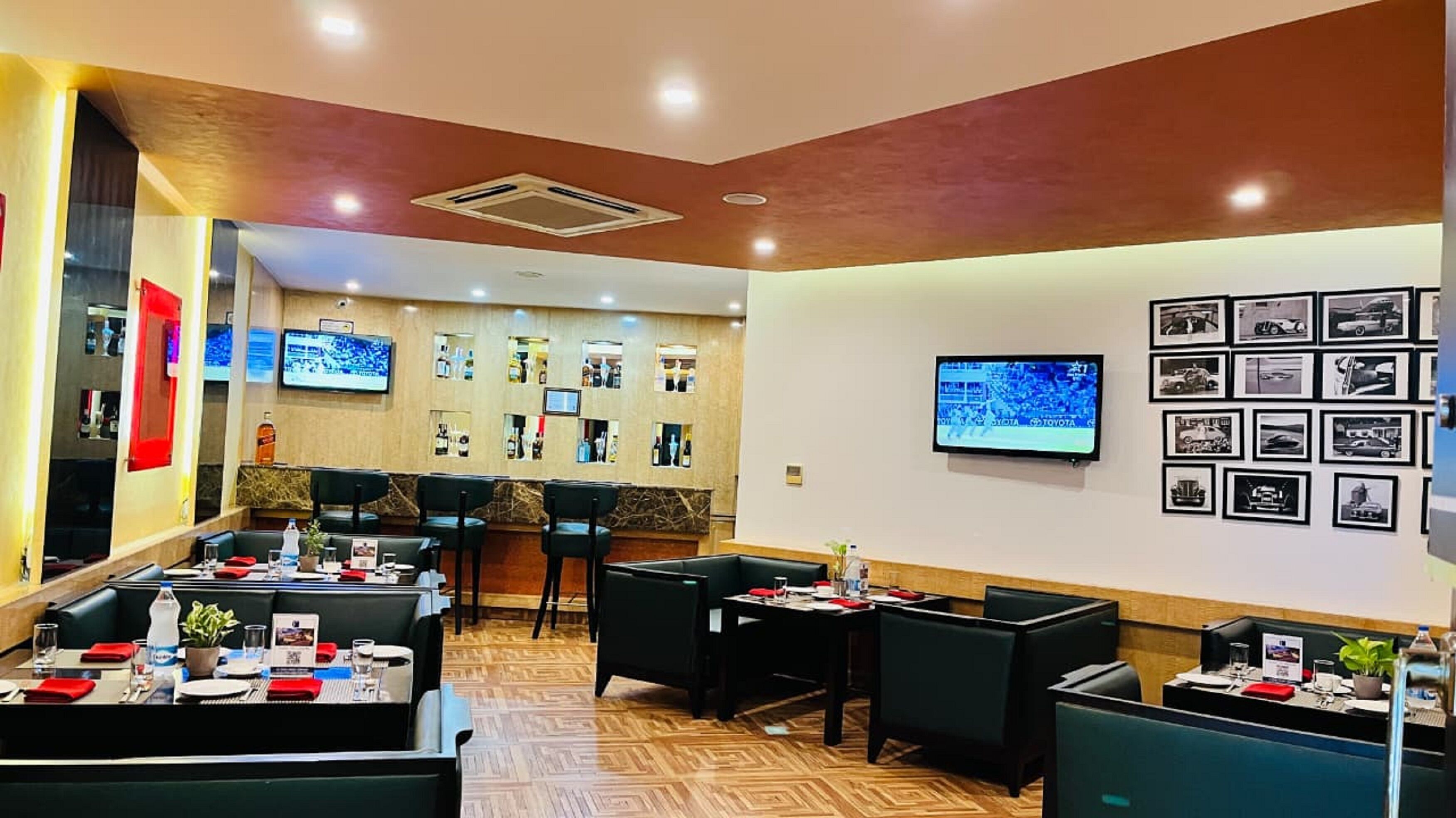 A restaurant with booths and tables, a bar area, and a wall with framed pictures and a TV screen.