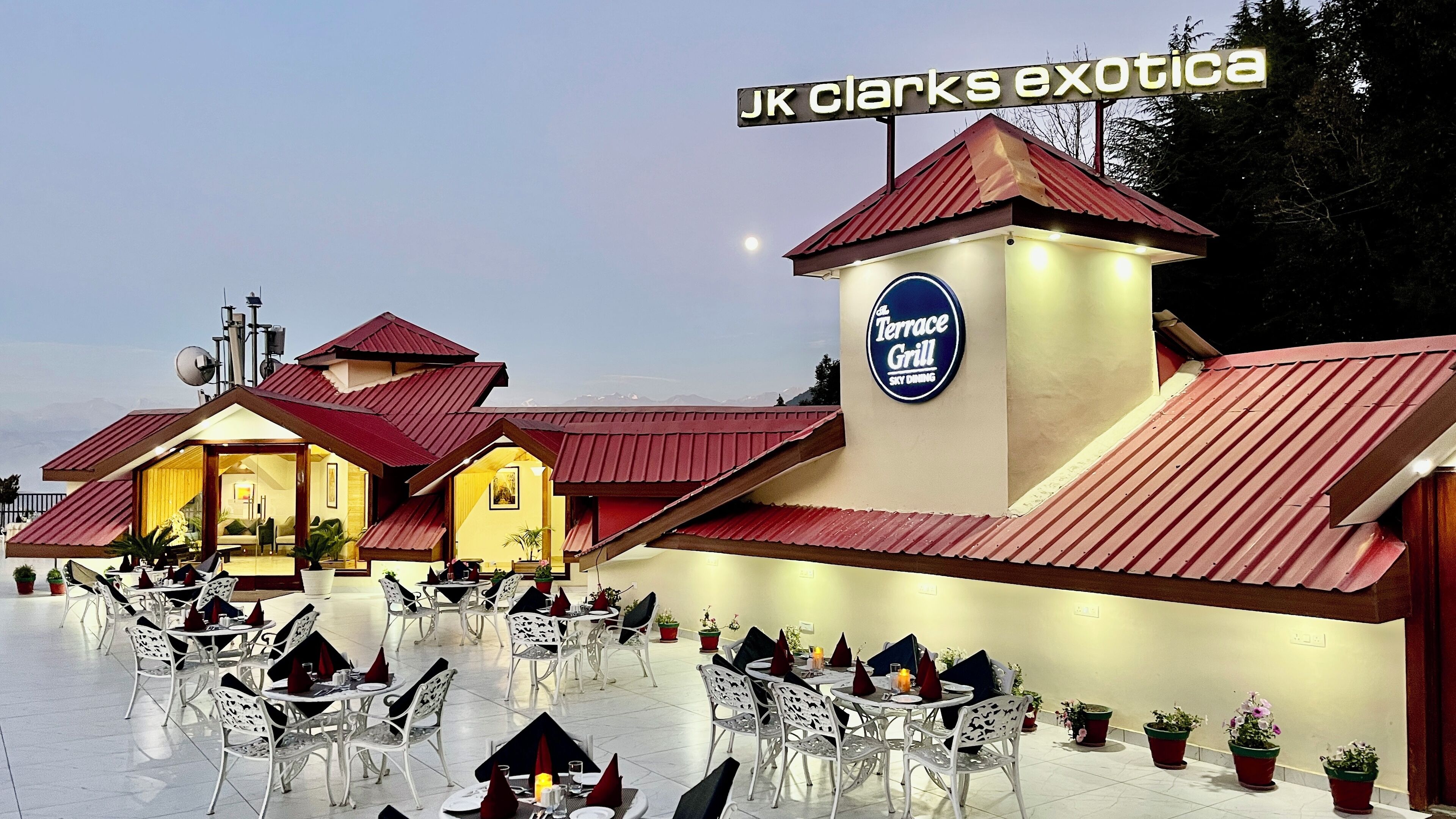 Un restaurante con terraza, una parrilla y el paisaje de montañas al fondo.