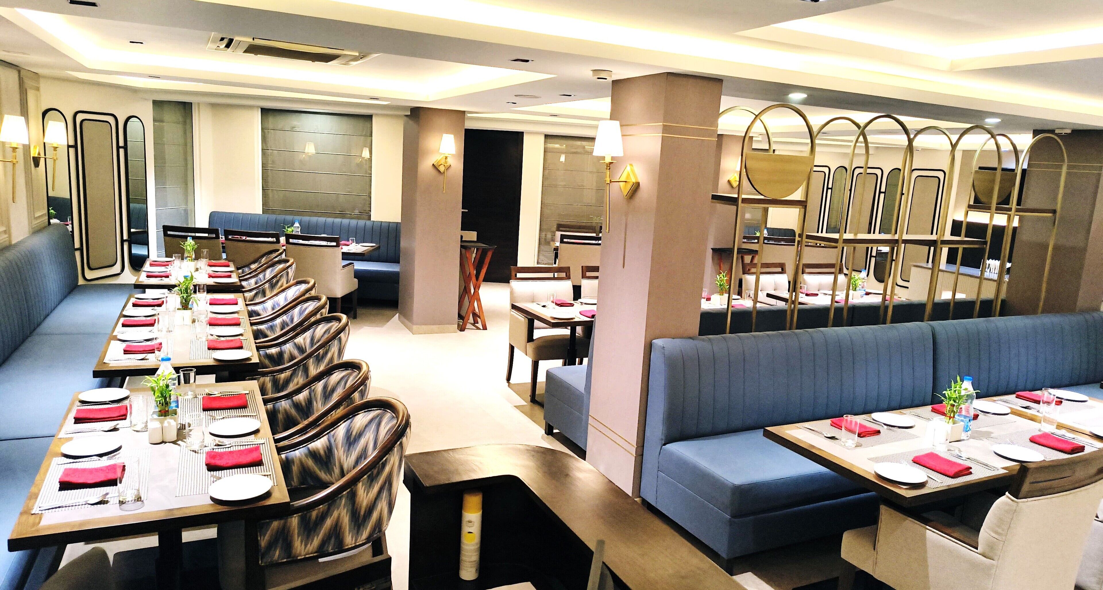A modern restaurant with long tables set for dining, cushioned seating, and contemporary decor.