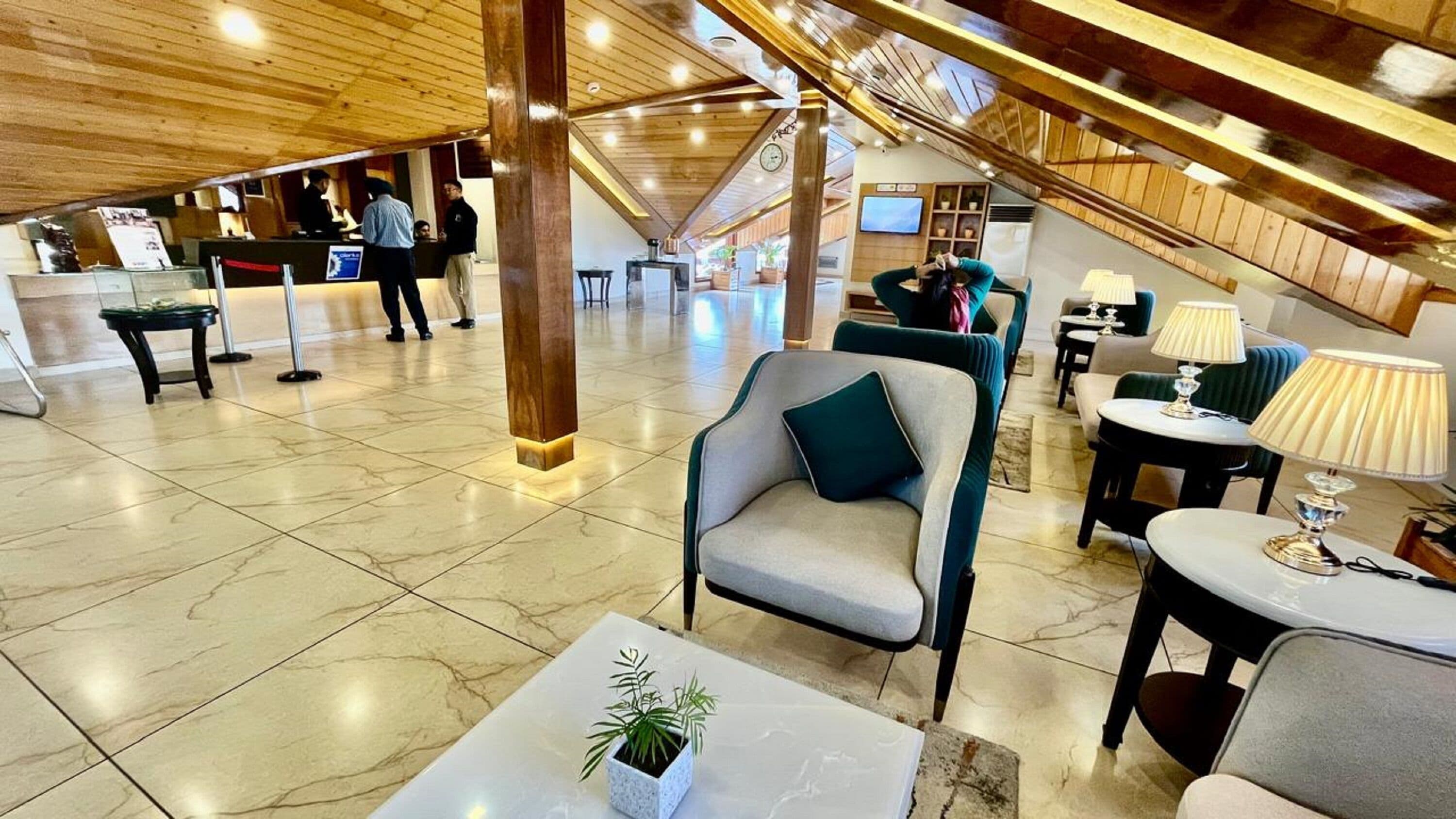 A spacious lobby with a high ceiling, a reception desk, seating area with tables and chairs, and a staircase leading to upper floors.