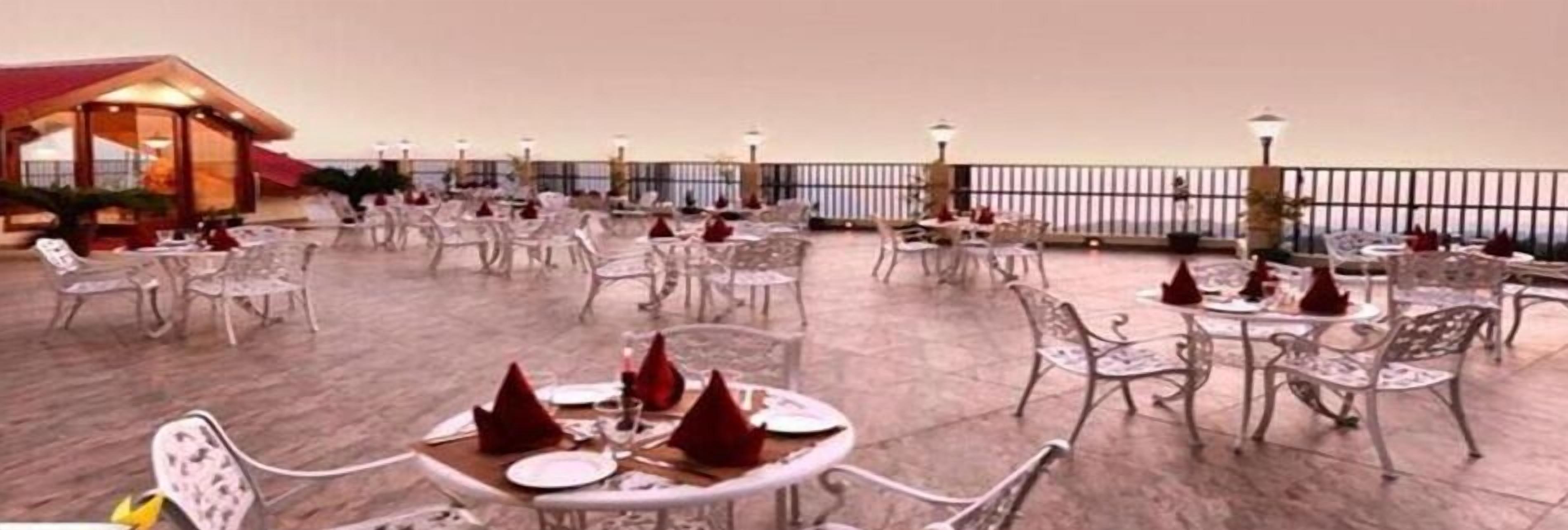 A rooftop dining area with round tables and chairs, a railing, and a view of the sea.