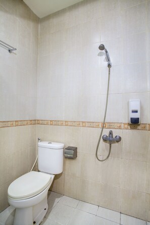 A bathroom with a toilet, a shower, and a soap dispenser on the wall. - Belvena Hotel (Jakarta)