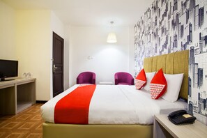 A hotel room with a bed, two chairs, a desk with a TV, and a telephone. - Belvena Hotel (Jakarta)