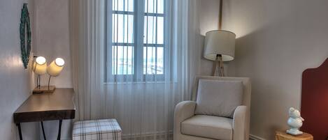 Una habitación con ventana, lámpara, silla, una mesita y un objeto decorativo.