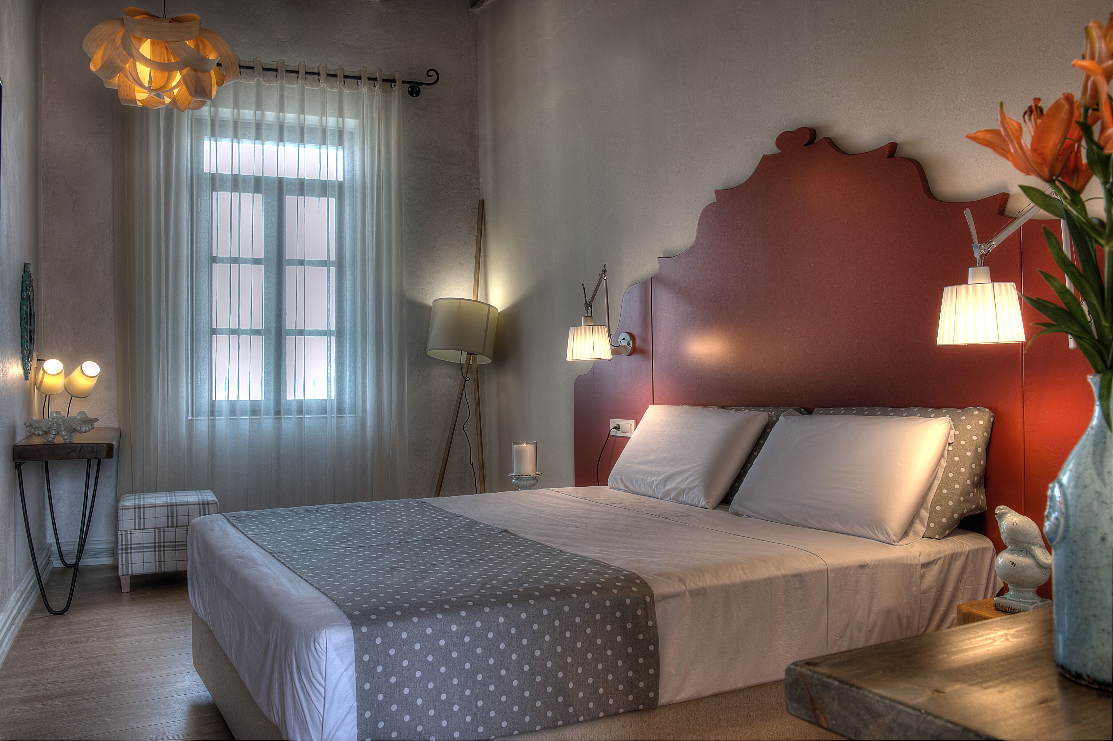 A bedroom with a bed, bedside lamps, a nightstand, a window with curtains, and a vase with flowers.