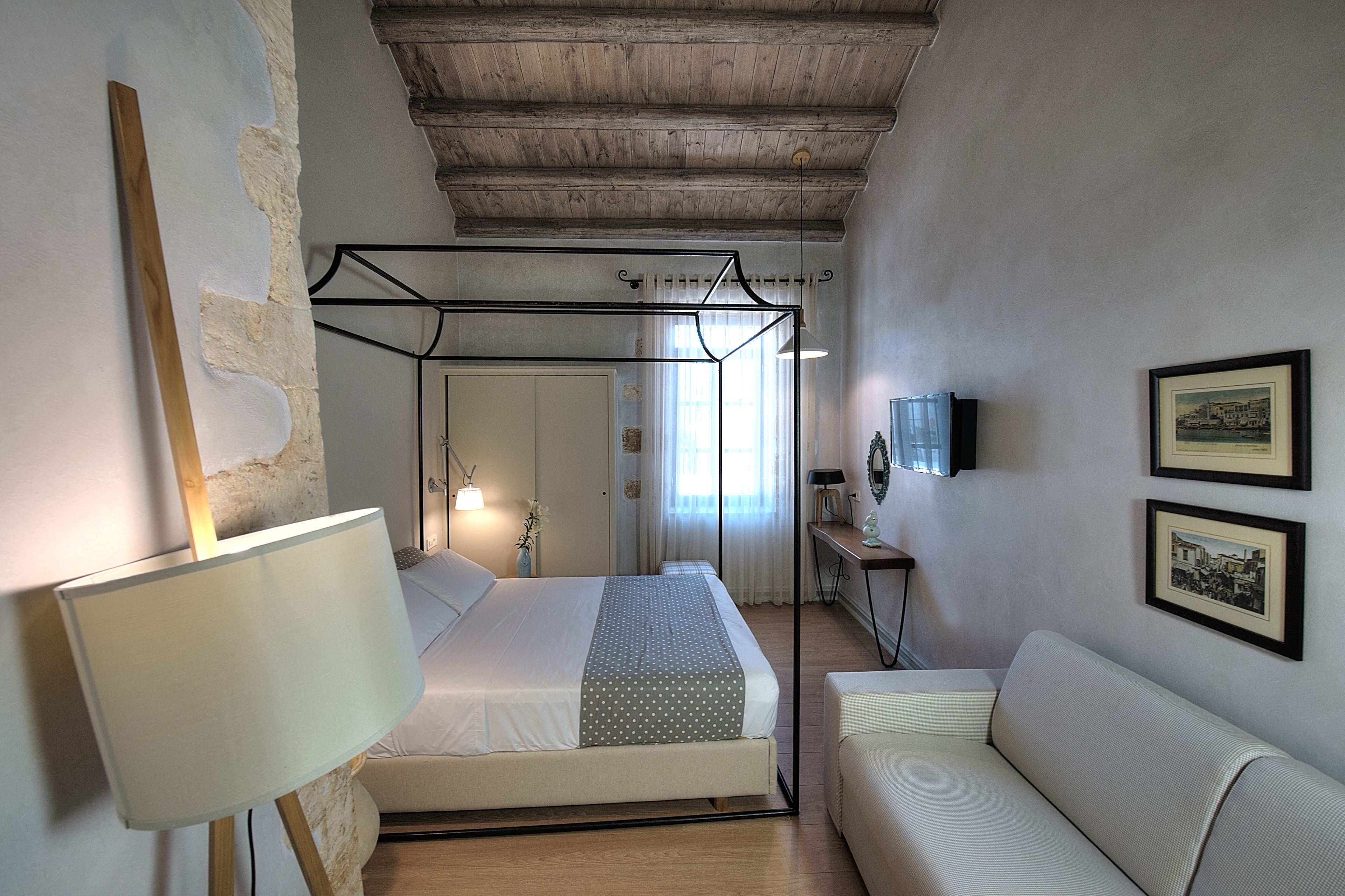 A bedroom with a bed, a bedside table, a lamp, a sofa, and framed pictures on the wall.