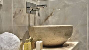 Un baño con un lavabo de mármol grande, un grifo cromado y diversos artículos de aseo en la encimera.