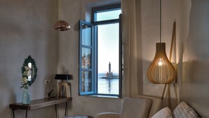 Een hotelkamer met een bed, een stoel, een klein tafeltje met een vaas, een lamp en een raam met uitzicht op een vuurtoren.