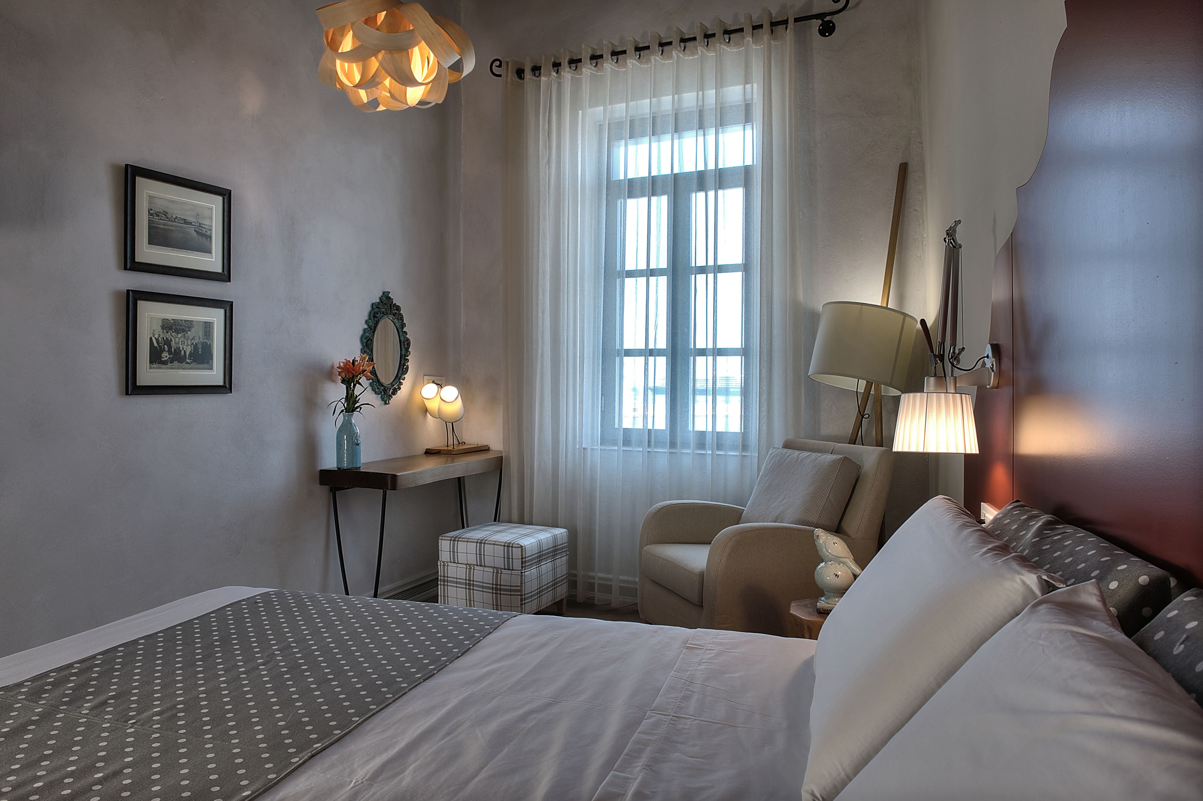 A hotel room with a bed, a chair, a desk with a lamp, and a window with curtains.