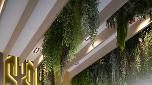 Un área de espera moderna con sillones reclinables, un diseño de pared geométrico y plantas colgantes.