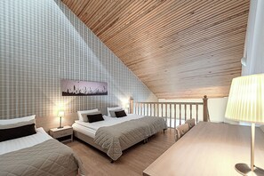 Un dormitorio con techo inclinado, una cama con colcha acolchada, mesitas de noche con lámparas y una obra de arte colgada en la pared.