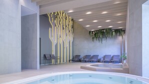 Un área de piscina interior moderna con un diseño de pared geométrico, sillones de descanso y un jacuzzi.