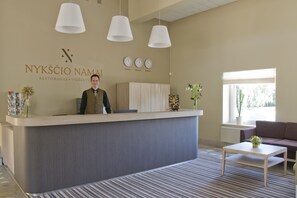 Zona de recepción con mostrador, recepcionista, reloj y ventana con planta.