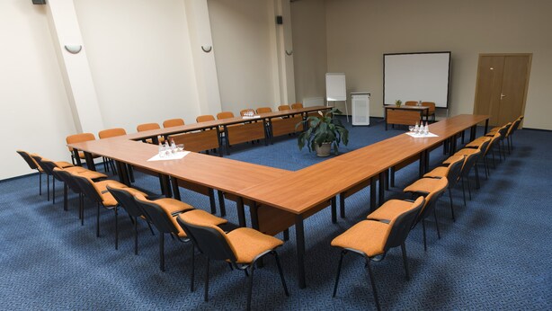 Un salón de conferencias con una larga mesa, sillas, una pizarra y una pantalla para proyector.