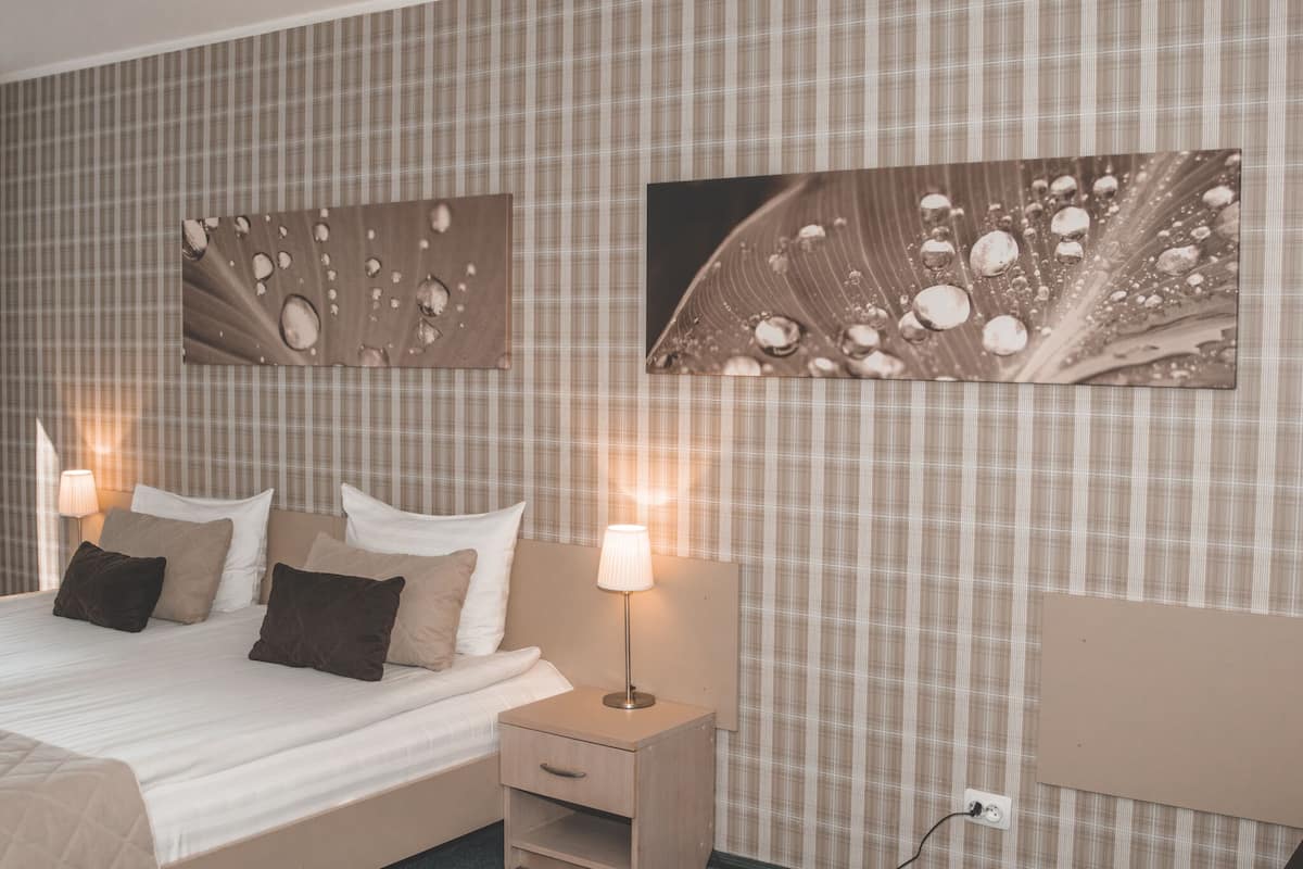 Una cama bien hecha con una mesita de noche de madera y una lámpara, una pared con estampado escocés y dos cuadros enmarcados.