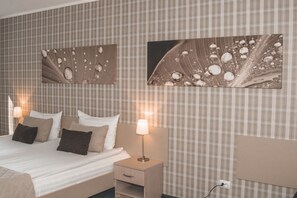 Una cama bien hecha con una mesita de noche de madera y una lámpara, una pared con estampado escocés y dos cuadros enmarcados.