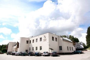 Un bâtiment doté d’un toit plat et de nombreuses fenêtres, portant l’inscription « Nykcso Namai ». Plusieurs voitures sont garées devant.
