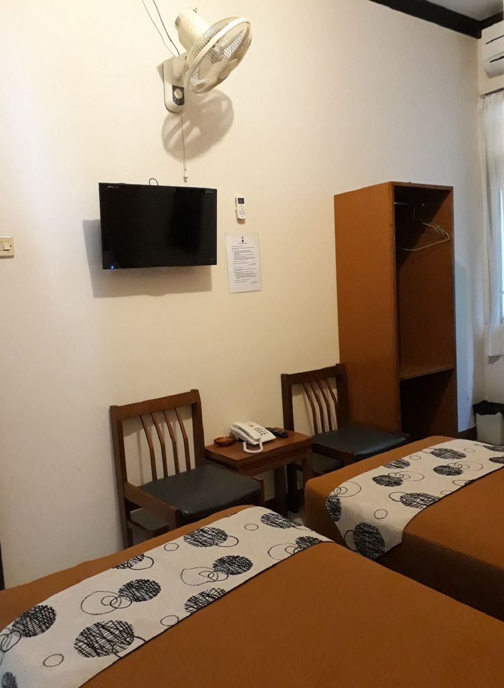 Ein Hotelzimmer mit zwei Betten, einem Fernseher, einem Schreibtisch mit Telefon und einem Kleiderschrank.