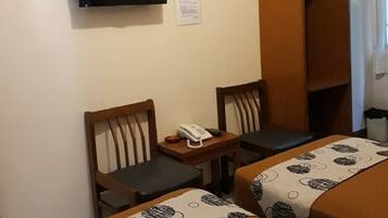 A hotel room with two beds, a television, a desk with a telephone, and a wardrobe.