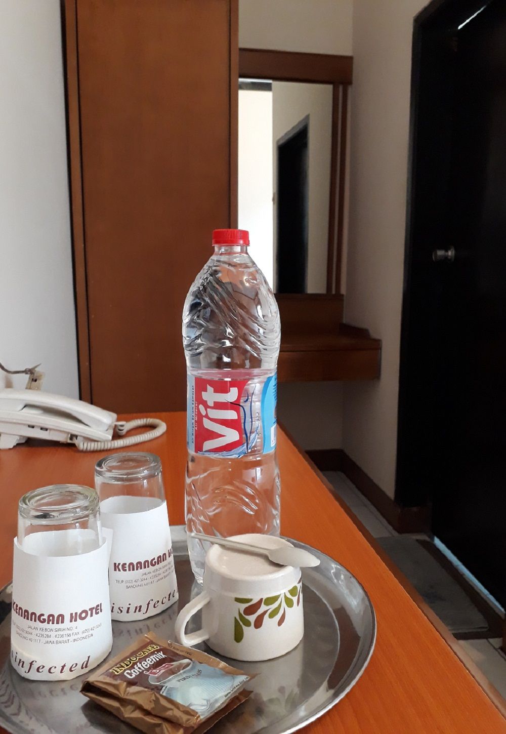 Ein Hotelzimmer mit Minibar, einer Vittel-Flasche, einer Tasse mit Löffel und einem Tablett mit Kaffeeremler.