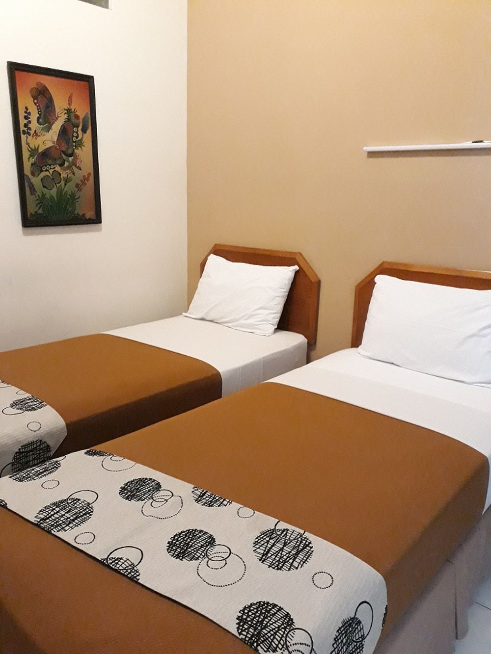 A hotel room with two single beds, each with a brown bedspread and white pillow. There is a painting on the wall above the beds.