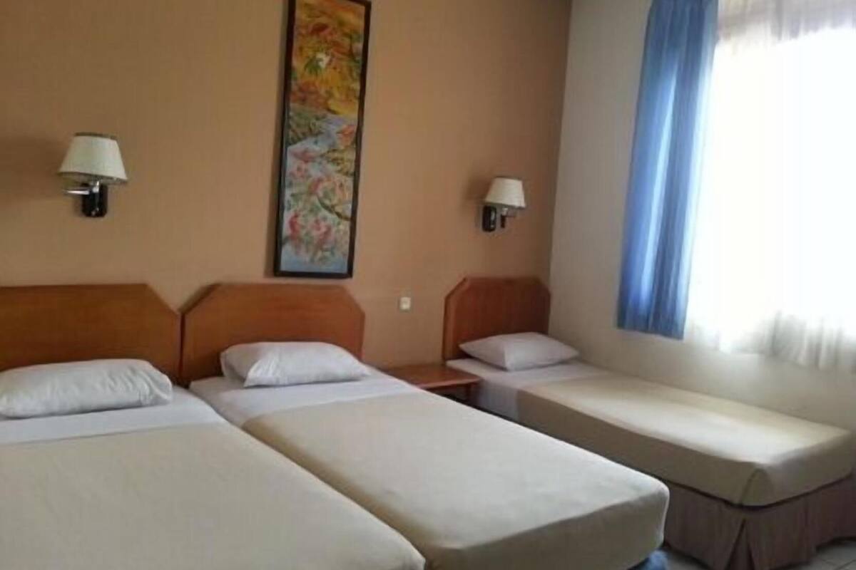 A hotel room with two single beds, a nightstand with a lamp, a painting on the wall, and a window with curtains.
