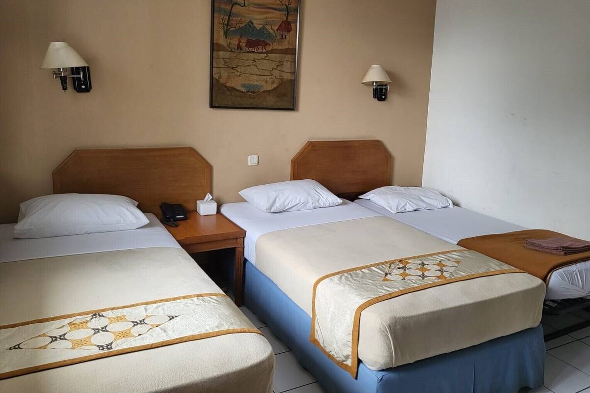 A hotel room with two beds, a wooden headboard, a painting on the wall, and two wall-mounted lamps.