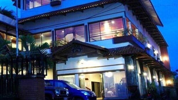 Un edificio de varios pisos con techo plano y amplias ventanas. Dos coches estacionados adelante.