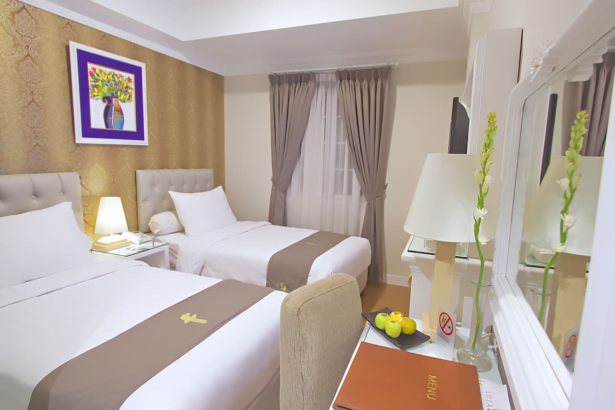 Habitación de hotel con dos camas, un escritorio con lámpara, un espejo y un cuadro en la pared.