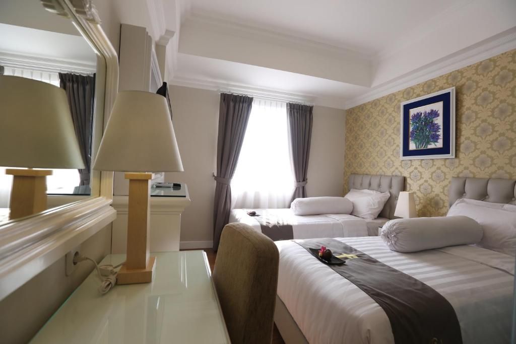 A hotel room with two beds, a desk, a lamp, and a window with curtains.