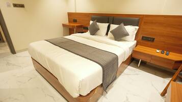 Una cama bien tendida con cabecera de madera, una mesita de noche con teléfono y control remoto, y un suelo con diseño de mármol.