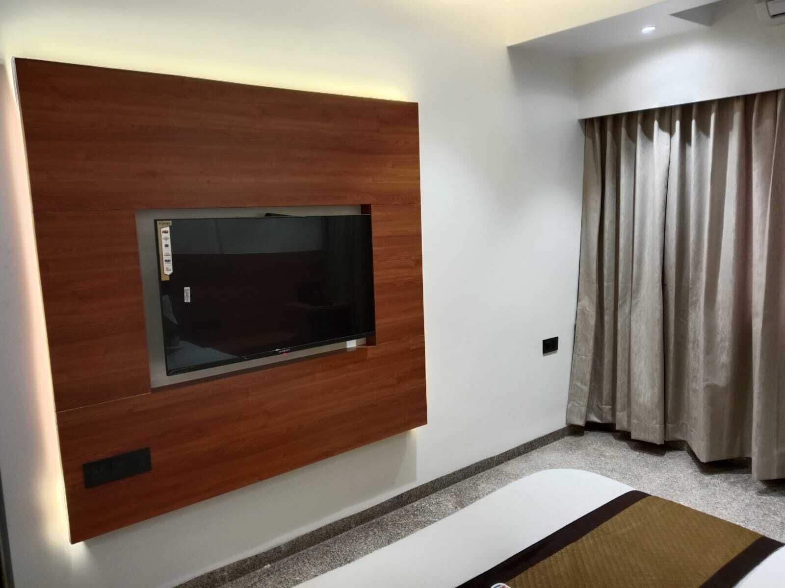 A modern room with a built-in TV, a wooden accent wall, a large window with curtains, and a carpeted floor.
