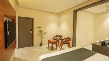 Habitación de hotel con cama, escritorio, dos sillas, televisor, planta en maceta y mostrador de recepción.