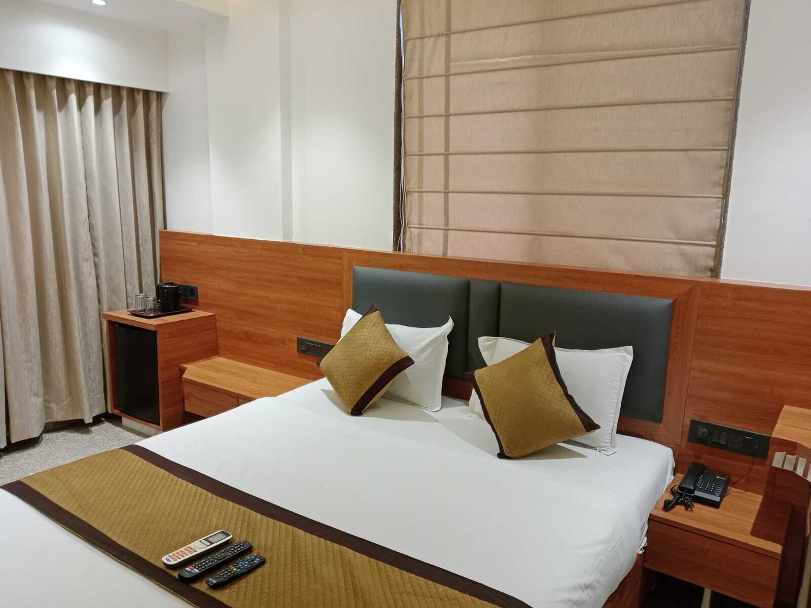 Habitación de hotel con una cama grande, dos mesitas de noche, un teléfono en la mesita y un control remoto sobre la cama.