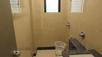 A bathroom with a toilet, sink, and shower. There is a window above the toilet and a shelf with towels.