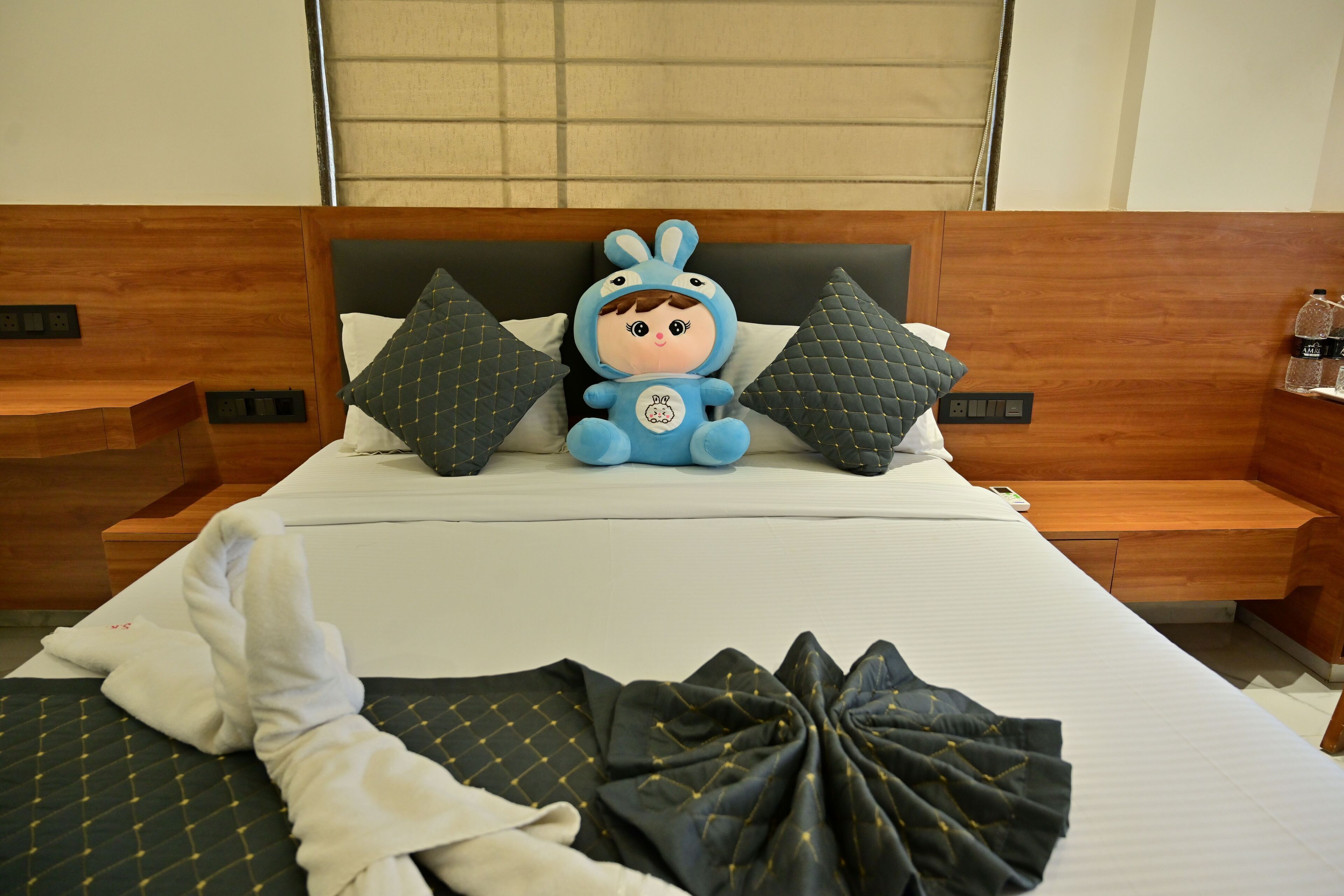 Una habitación de hotel con una cama, un peluche y una toalla doblada con cuidado.