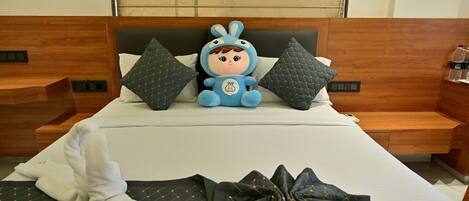 Una habitación de hotel con una cama, un peluche y una toalla doblada con cuidado.