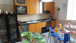 A compact kitchen with wooden cabinets, a built-in oven, a sink, and a dining area with a table and chairs. - Melone Giallo (Paceco)