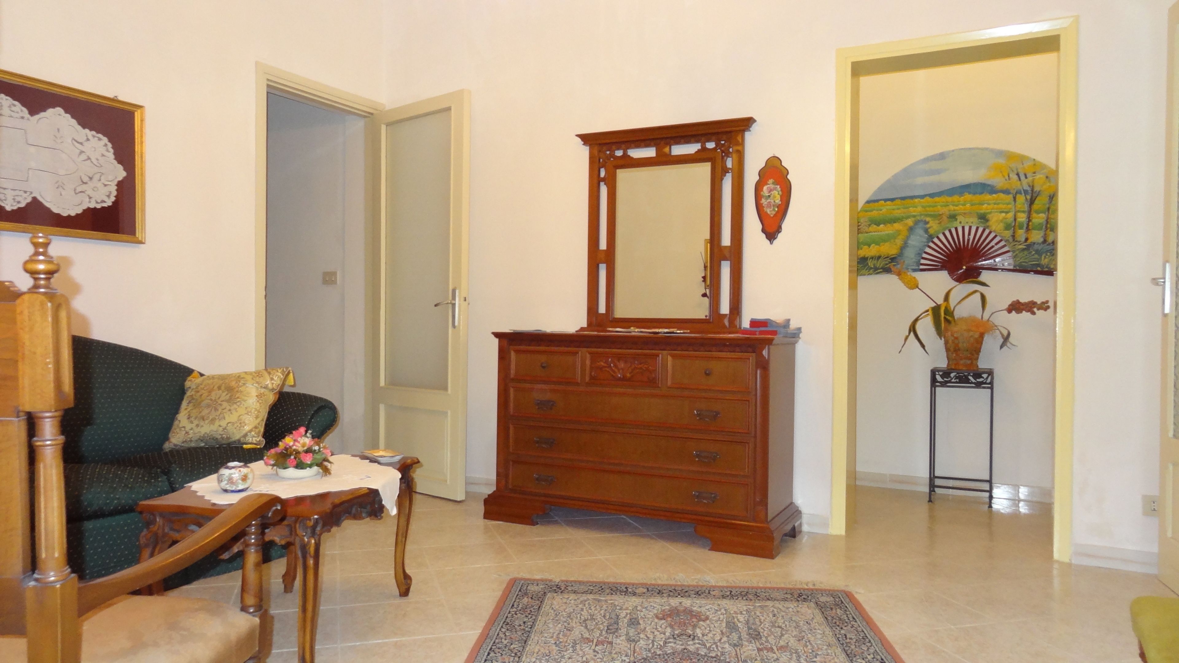A living room with a wooden dresser, a sofa, a small table with a vase, and a rug.