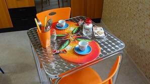A dining table with orange chairs, a colorful placemat, and a glass top. - Melone Giallo (Paceco)