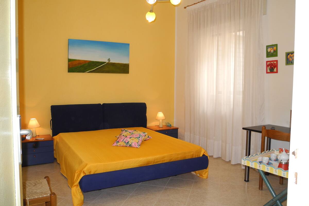 A bedroom with a bed, bedside tables, a lamp, a painting, and a table with items.