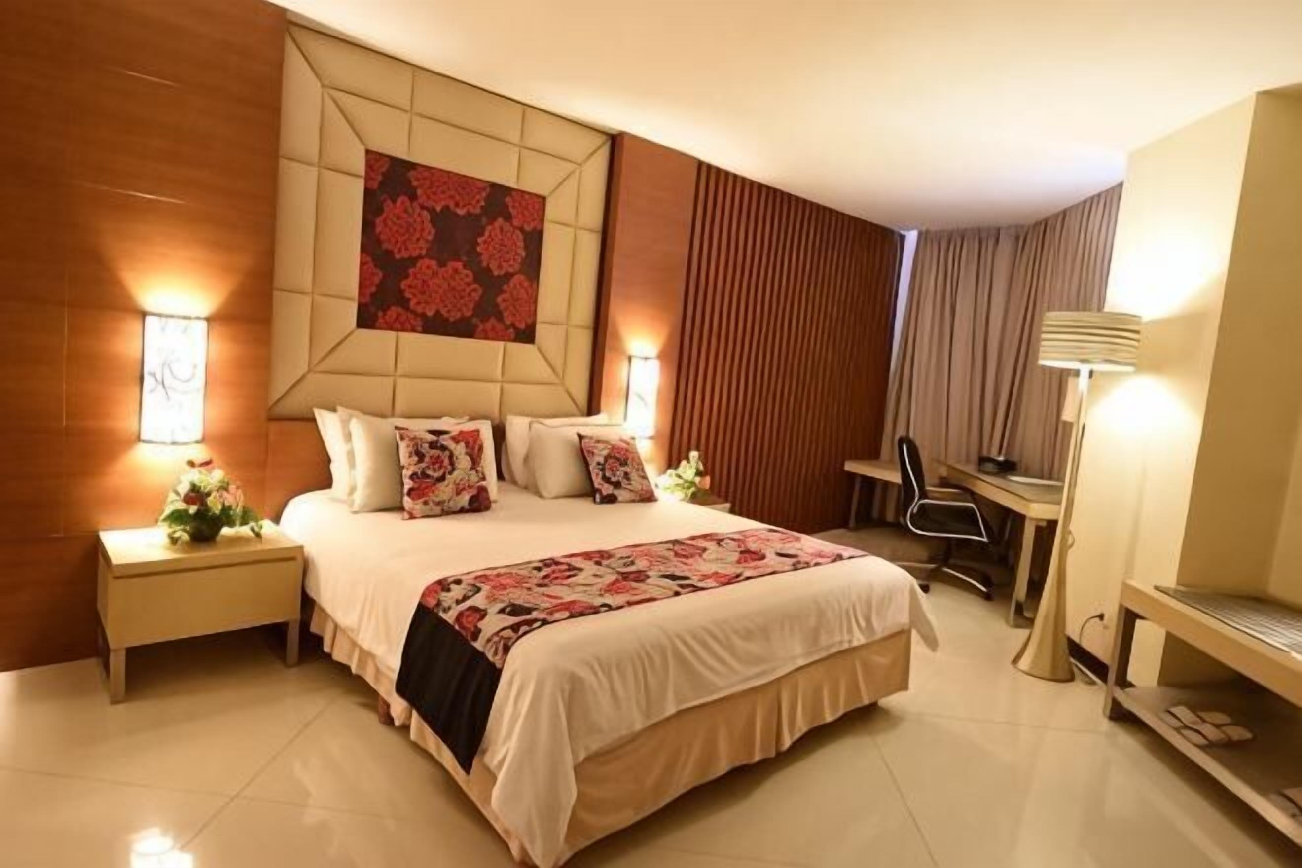 Una habitación de hotel con una cama grande, mesitas de noche, un escritorio, una silla y un televisor.