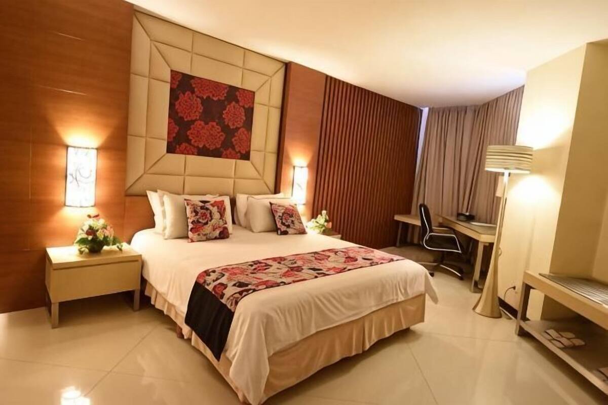 Una habitación de hotel con una cama grande, mesitas de noche, un escritorio, una silla y un televisor.