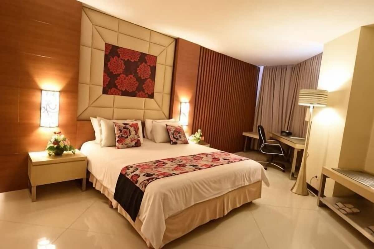 A hotel room with a large bed, bedside tables, a desk, a chair, and a TV.