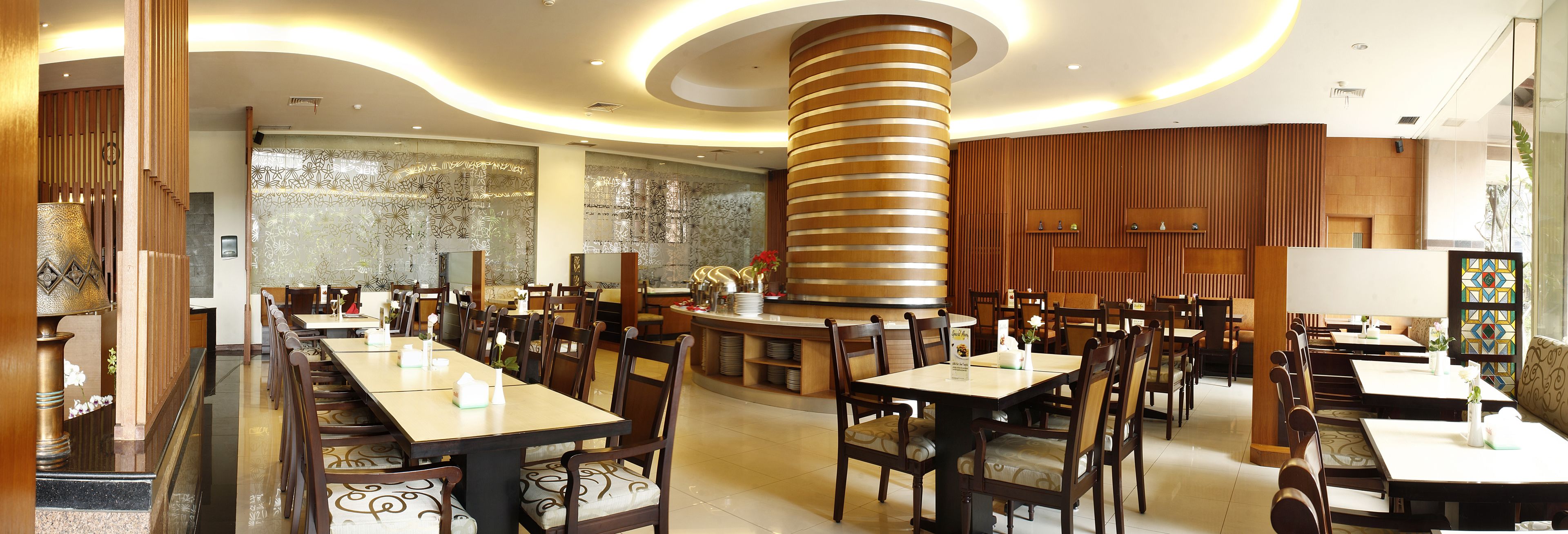 A spacious restaurant with multiple dining tables and chairs, a central column, and a decorative wall with a geometric pattern.