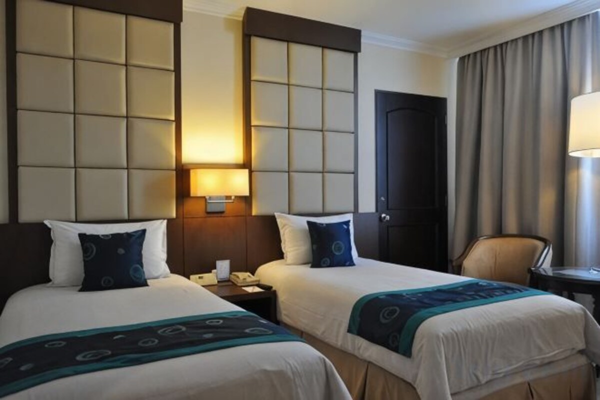 A hotel room with two beds, a nightstand, a lamp, and a door.