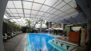 A swimming pool with a covered area, lounge chairs, and umbrellas. - Kedaton Hotel (Bandung)