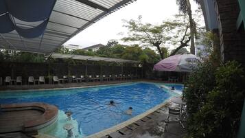 Una piscina con zona cubierta, sillas de descanso y una pequeña terraza.